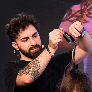 Mann frisiert Mann mit Rasierapparat auf einer Bühne